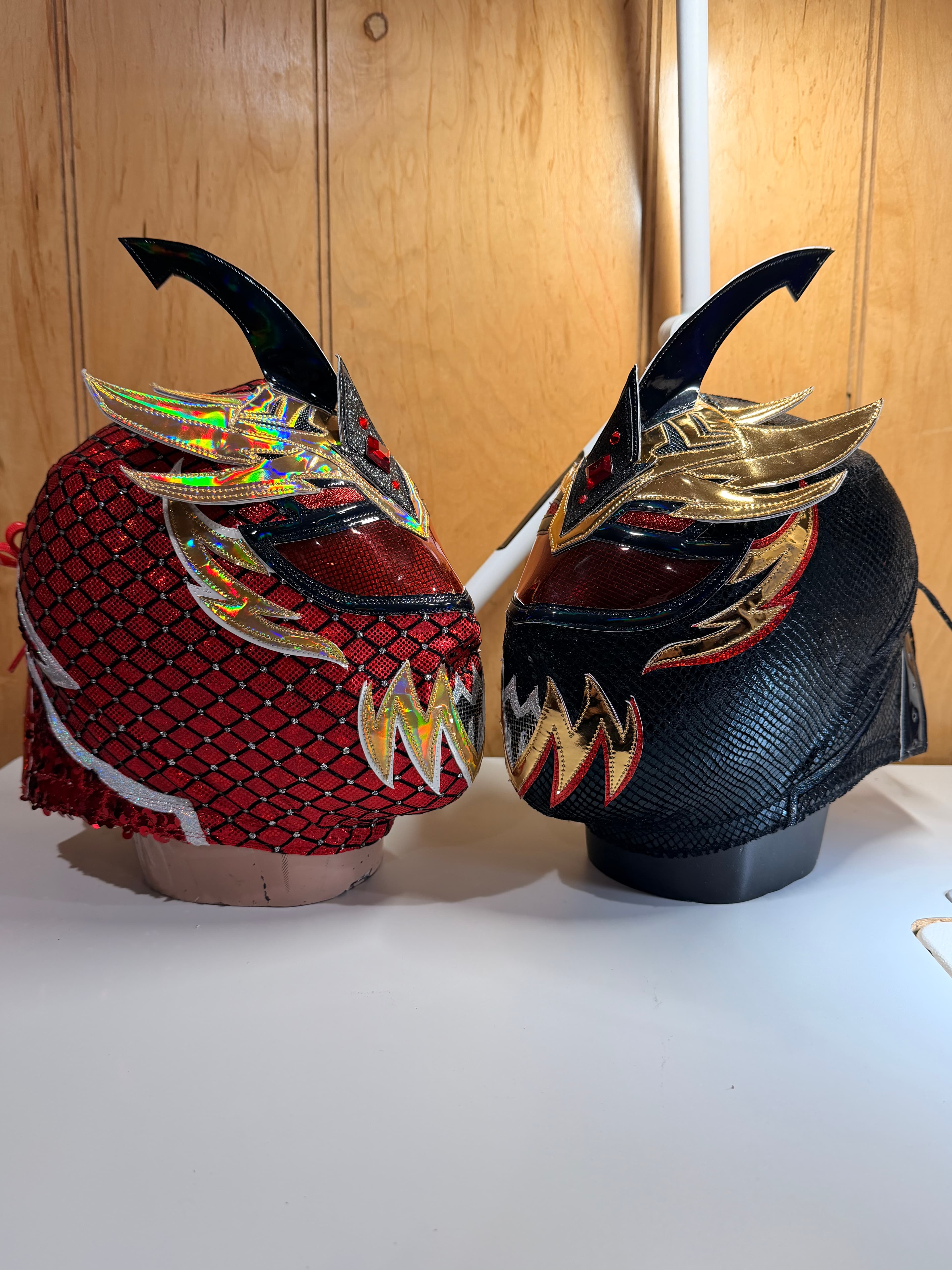 Two intricate luchador masks, one black and gold, one red with a diamond pattern.