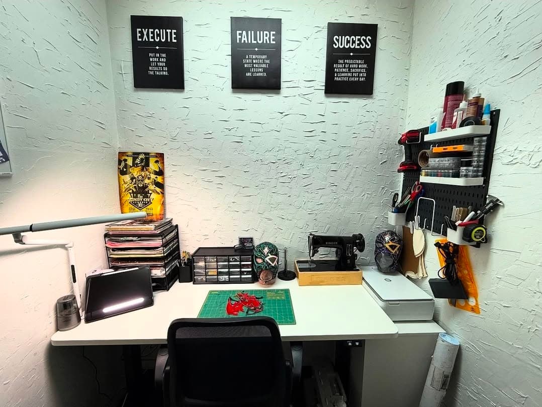 Organized sewing workspace with a desk, machine, and motivational posters on white textured walls.