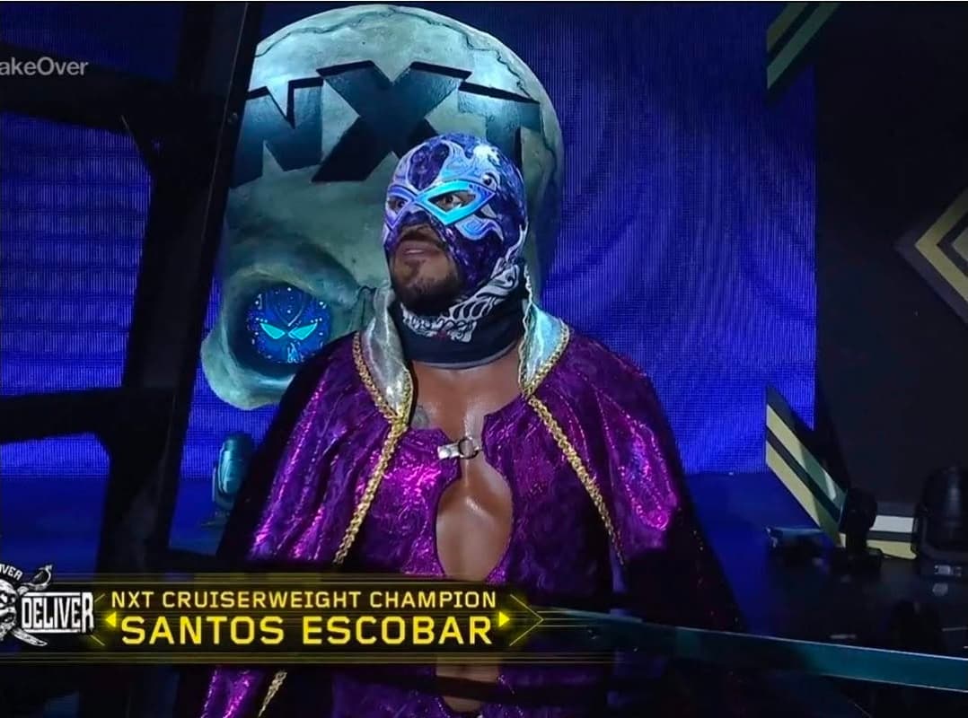 Masked wrestler Santos Escobar in a purple cape stands before a giant NXT skull backdrop.