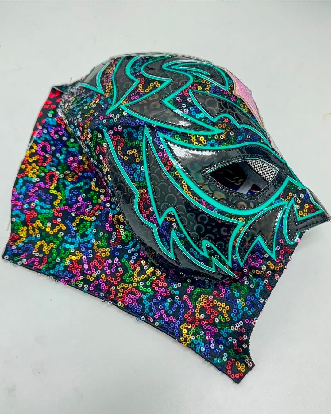 Vibrant rainbow sequined luchador mask featuring black vinyl and bright teal jagged flame designs.