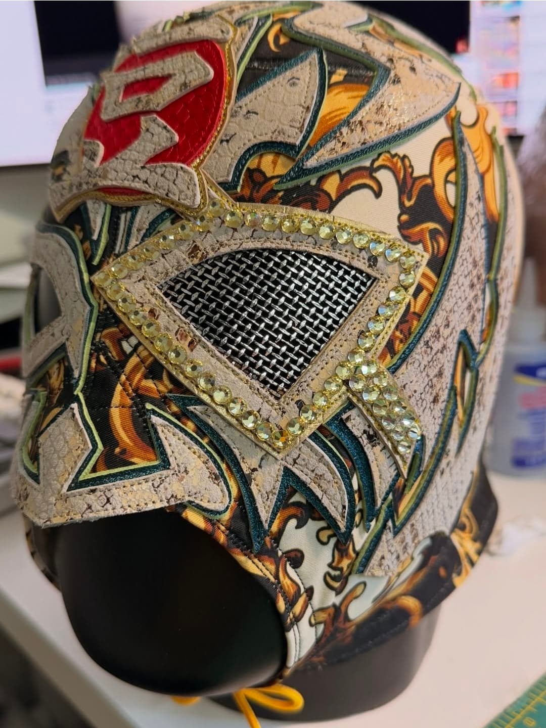 Intricate Lucha Libre mask with ornate patterns, mesh eye hole, and yellow rhinestone detailing.