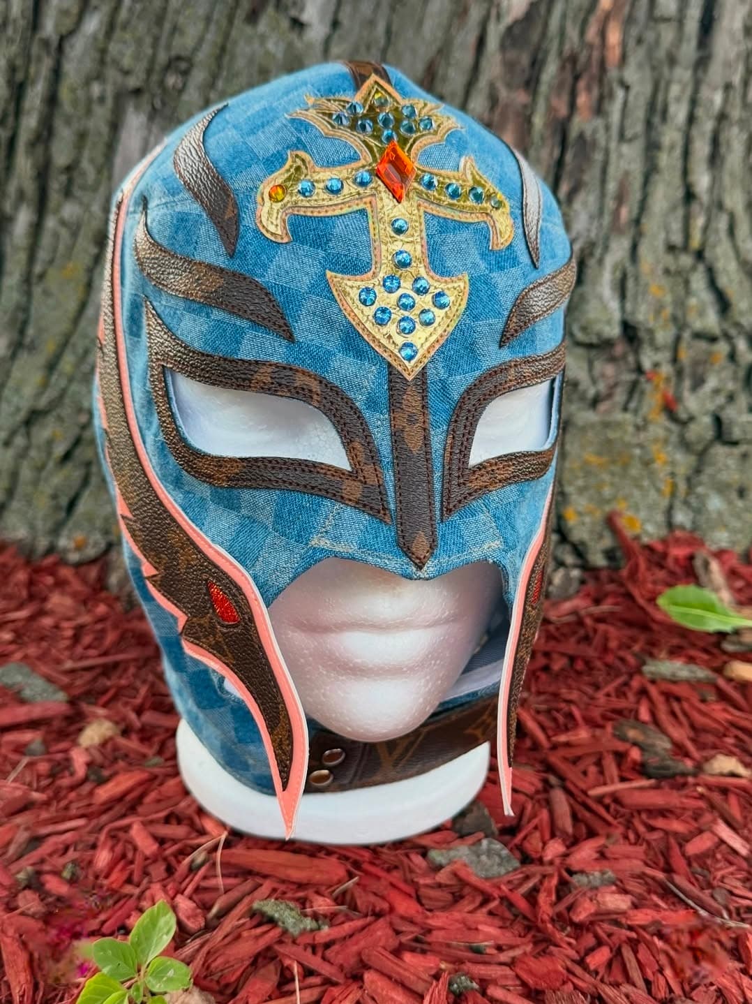 Blue checkered luchador mask with a jeweled gold cross and brown monogram leather accents.